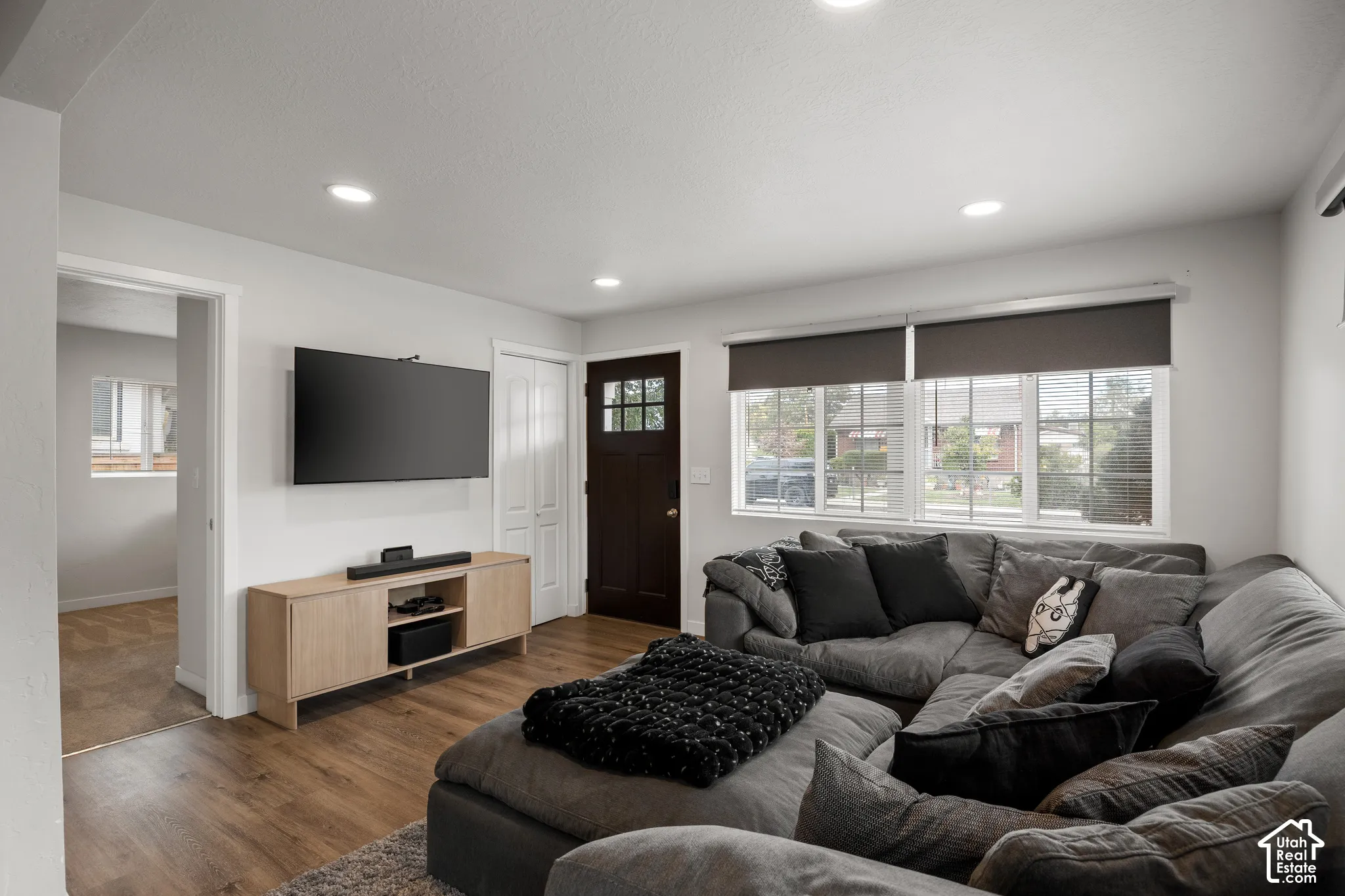 Living area featuring wood-finish flooring, recessed lighting, multi-pane windows, and a dark-toned entry door with glass pane detailing