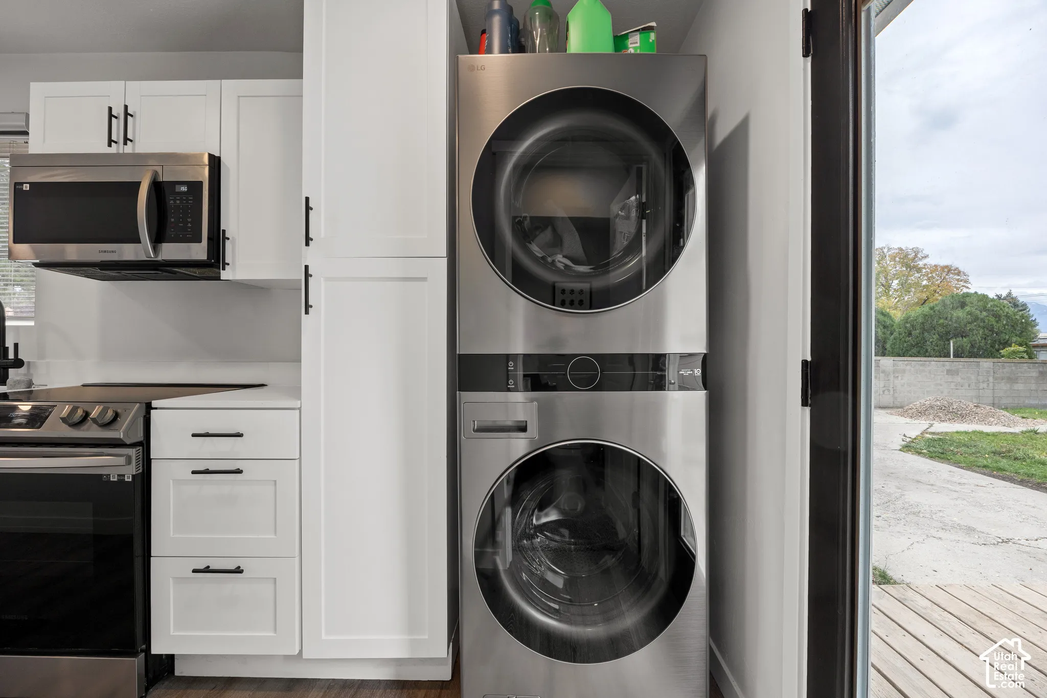 Stacked stainless steel laundry center, white shaker-style cabinetry with matte black hardware, and built-in microwave