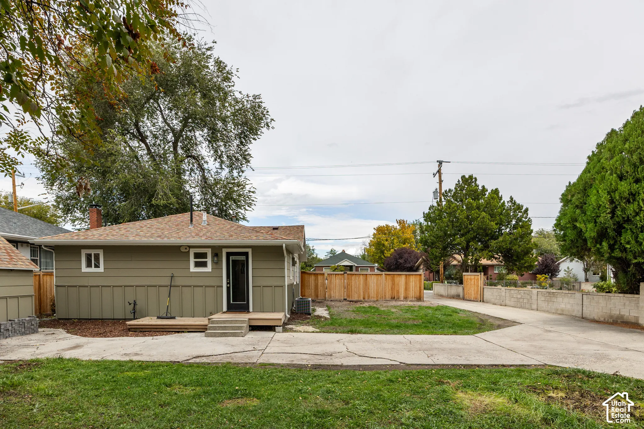 Exterior featuring board-and-batten siding, asphalt shingle roof, wood deck, concrete driveway, and wooden privacy fencing