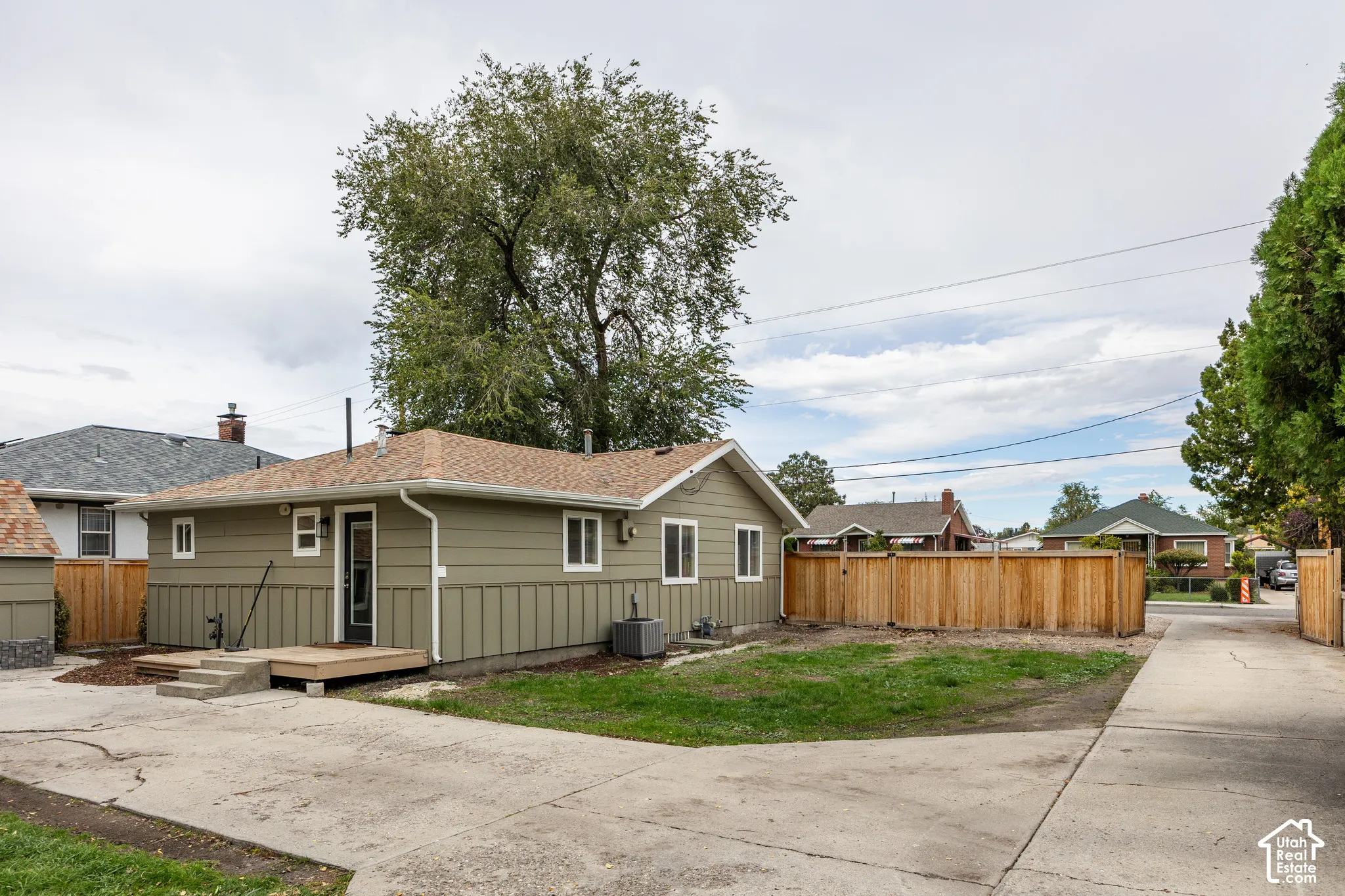 Exterior featuring horizontal and vertical siding, a composition shingle roof, a wood deck, a concrete driveway, and wood privacy fencing