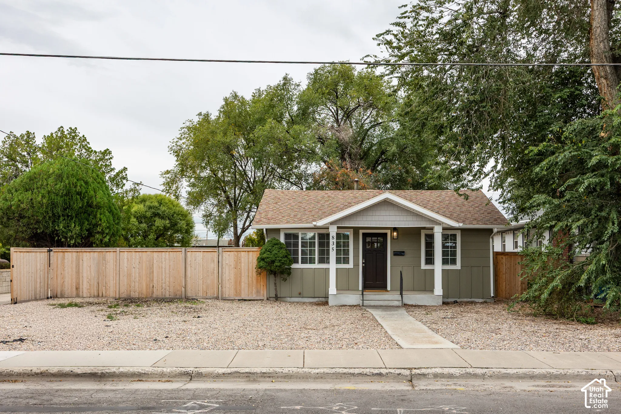 Single-story residence featuring vertical siding, a front porch with a gabled roof, multi-pane windows, and a wood privacy fence