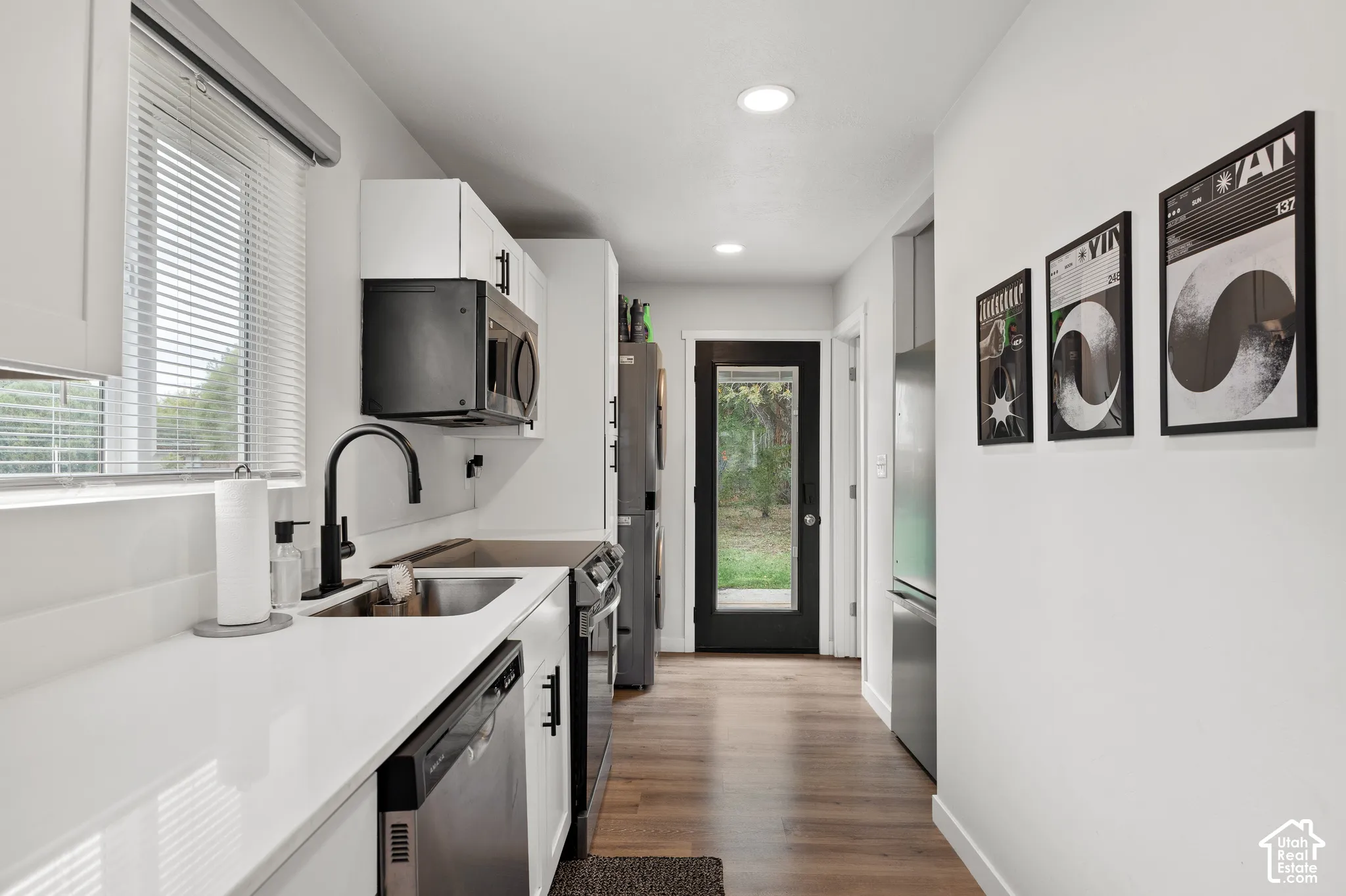 Kitchen featuring white cabinetry, solid-surface countertops, stainless steel appliances, a matte black high-arc faucet, and wood-finish flooring