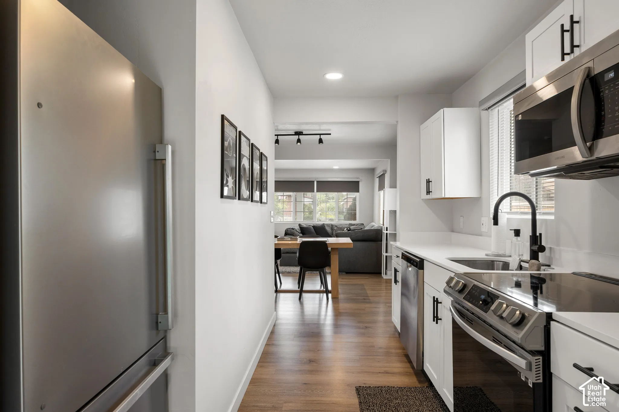 Kitchen featuring white shaker cabinetry, stainless steel appliances, wood-finish flooring, matte black hardware, and solid-surface countertops