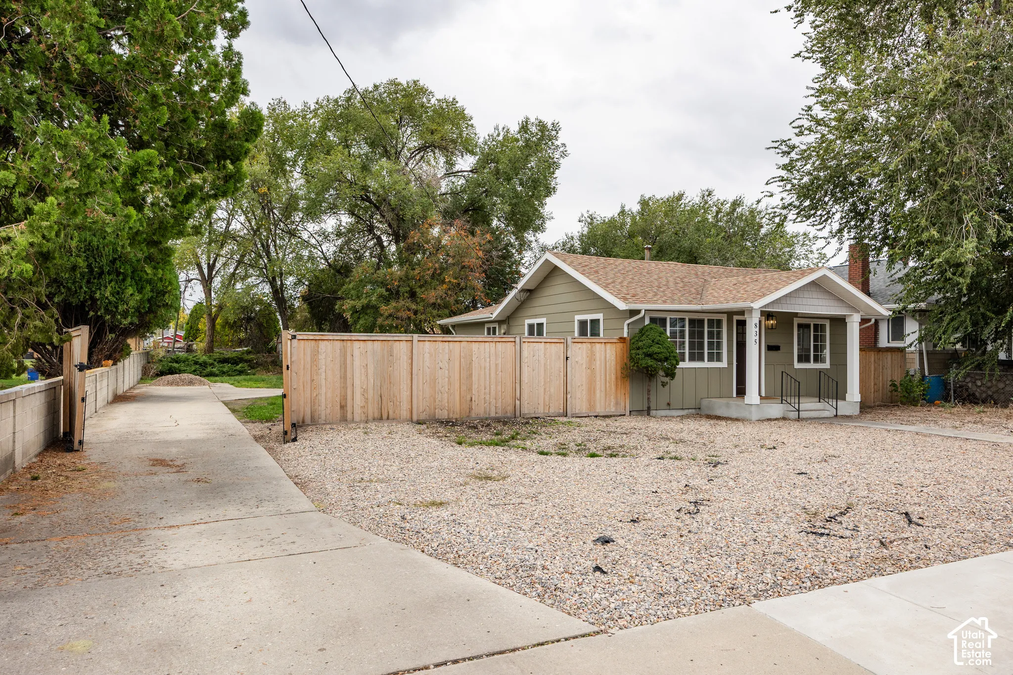 Single-story exterior with horizontal siding, covered front porch, gravel front yard, wood-panel fencing, and a concrete driveway