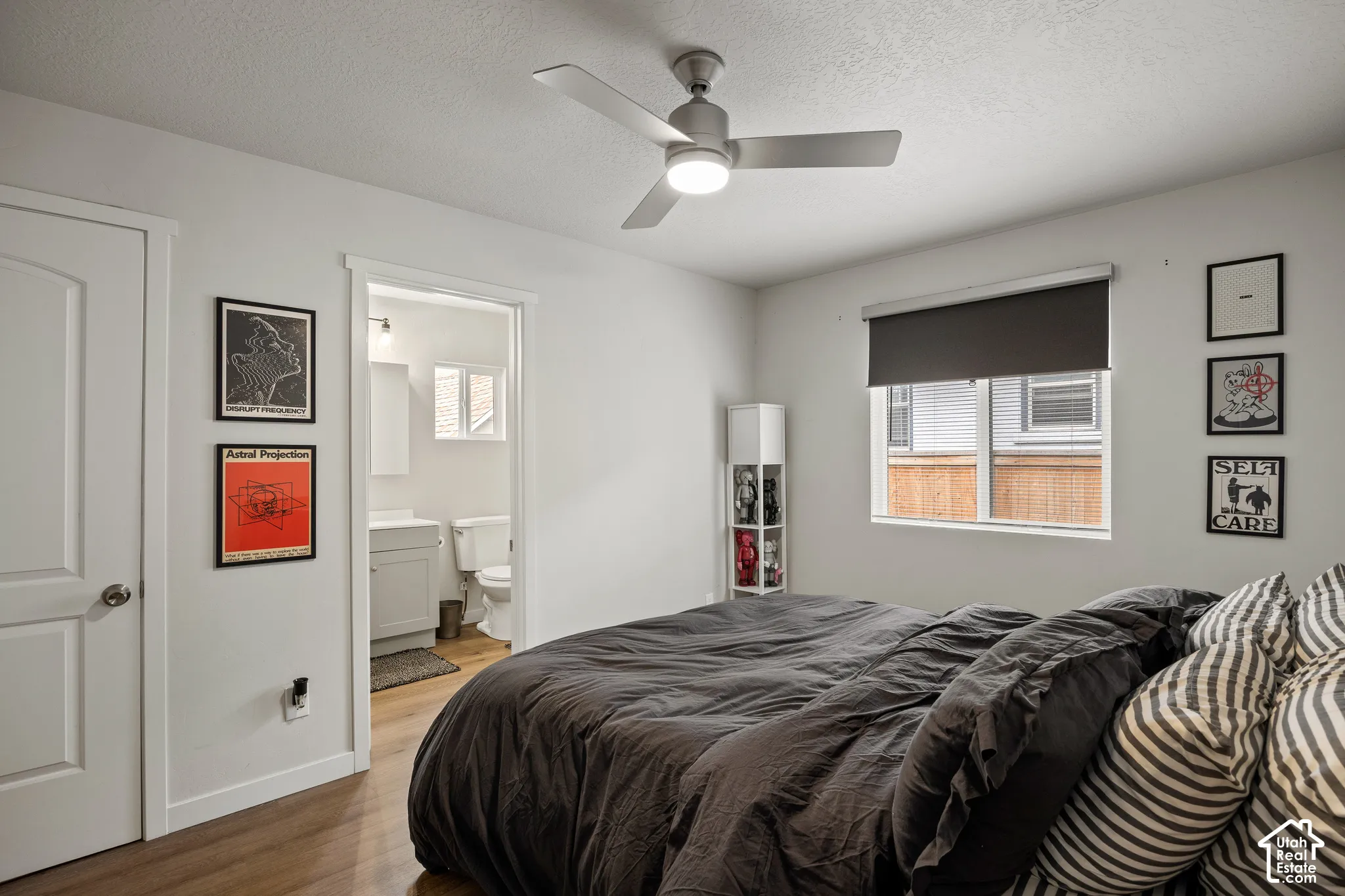 Room featuring wood-finish flooring, a matte nickel ceiling fan with integrated lighting, neutral wall paint, and a roller shade window treatment