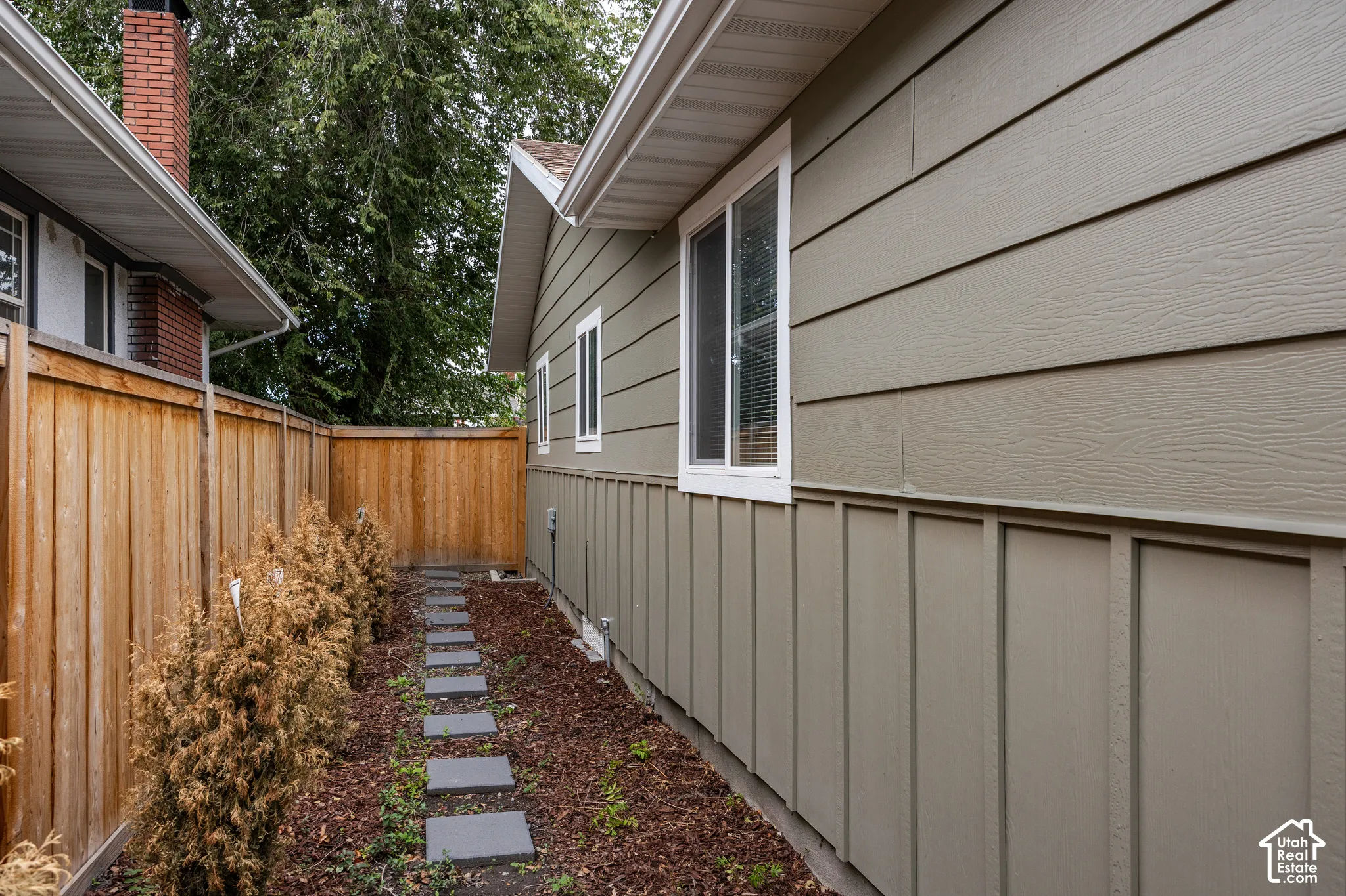 Exterior side yard featuring horizontal and board-and-batten siding, a wood privacy fence, and a stone paver walkway set in mulch