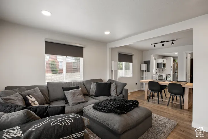 Open living area featuring wood-finish flooring, recessed lighting, and large windows with roller shades