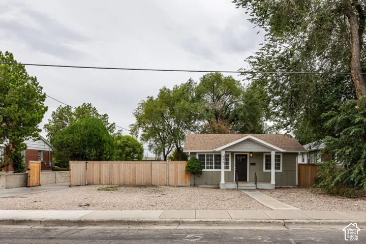Single-story home featuring wood-paneled siding, a gabled roofline, a concrete front porch with support columns, and privacy fencing
