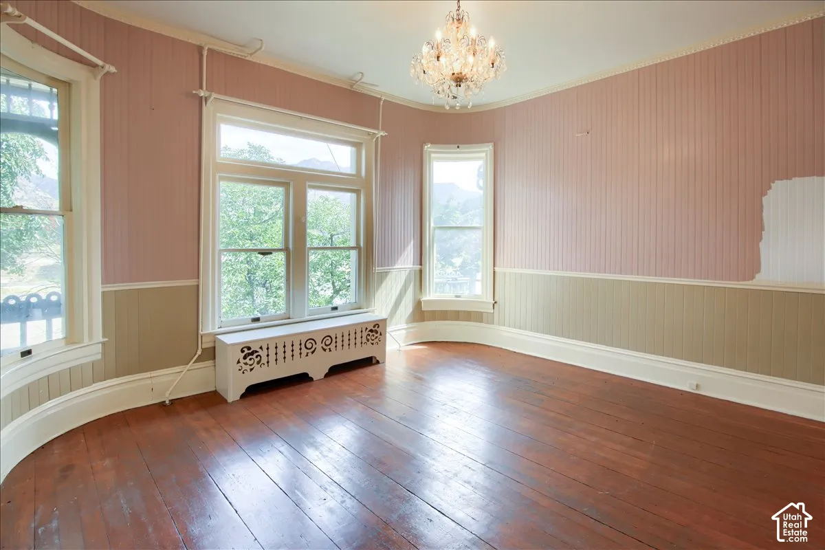 Rounded room featuring original hardwood flooring, beaded board wainscoting, multi-pane windows, a decorative radiator cover, and a crystal chandelier