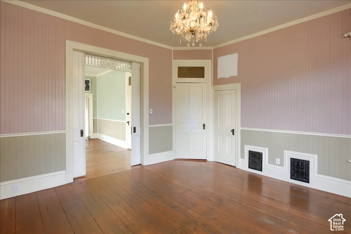 Interior space featuring wood-finish flooring, beadboard wall paneling, multi-panel wooden doors with transoms, and a crystal chandelier
