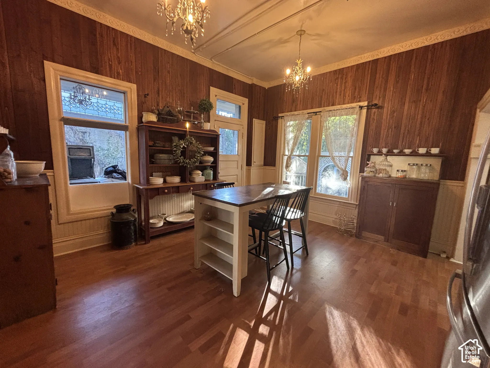 Wood-paneled walls, decorative crown molding, wood-finish flooring, and dual hanging chandeliers