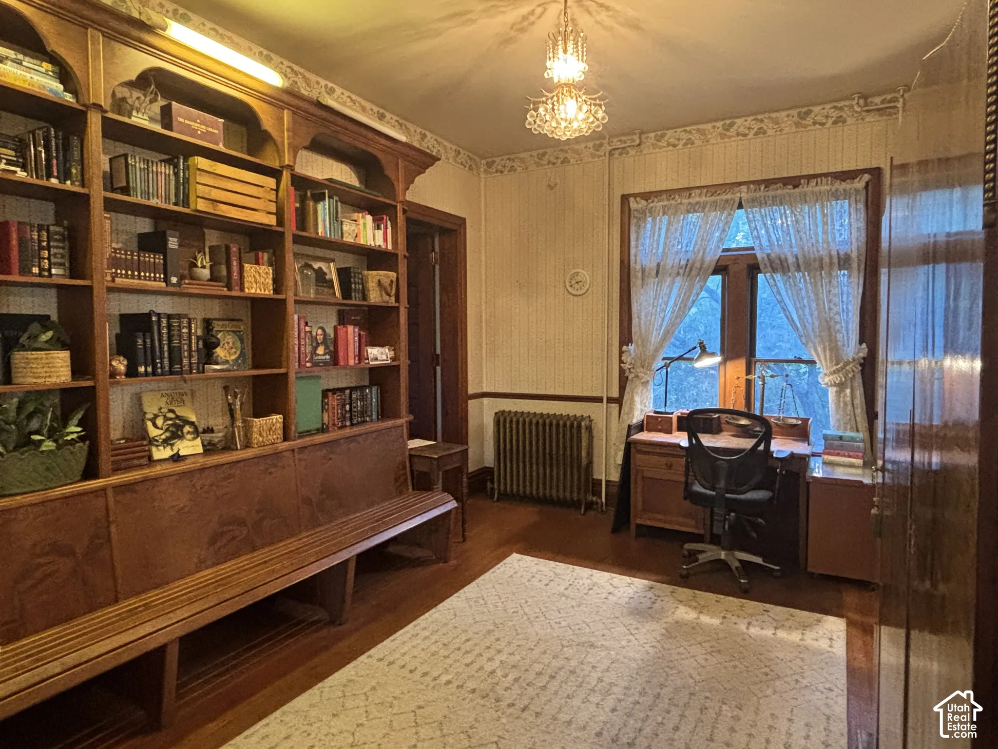 Floor-to-ceiling custom wood shelving with integrated bench seating, multi-pane windows, crystal chandelier, and cast-iron radiator