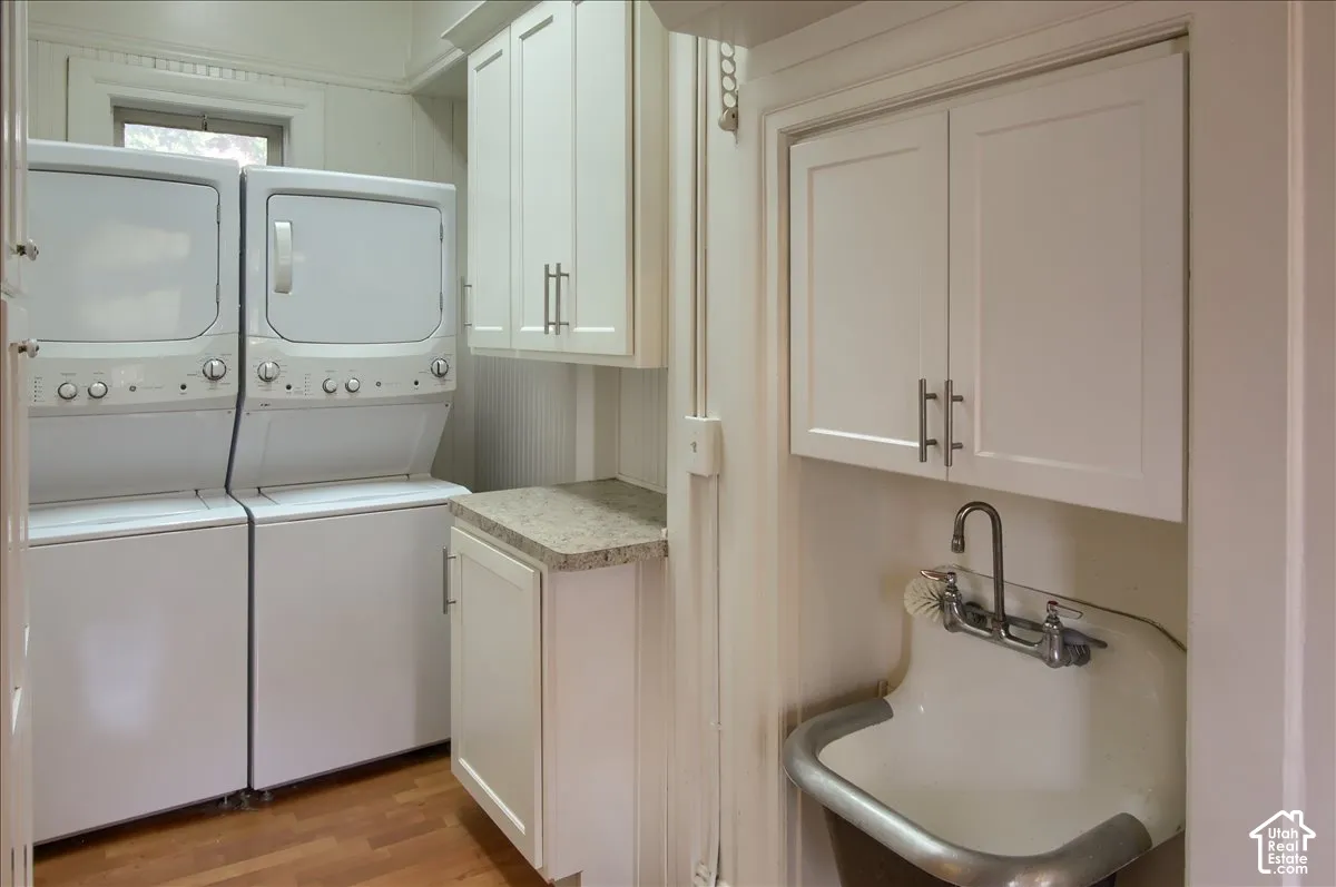 Utility area featuring white shaker-style cabinetry, stone-finish countertops, wall-mounted utility sink with metal rim, and wood-finish flooring