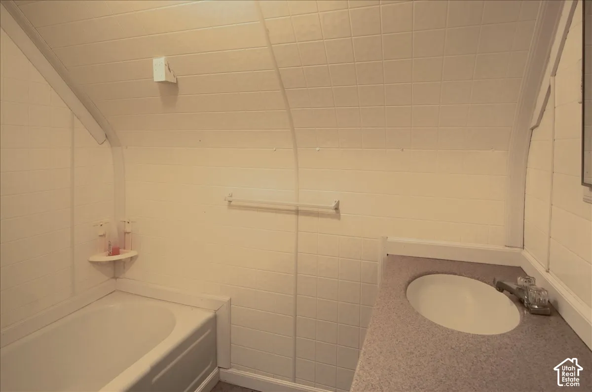 Curved wall and ceiling architecture with square tile surround, integrated bathtub, solid-surface vanity countertop with oval basin, and wall-mounted metal towel bar