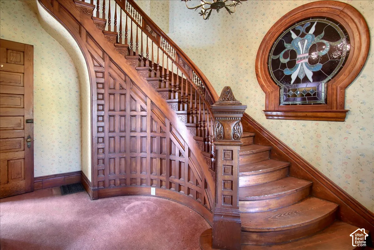 Curved staircase featuring intricate wood paneling, a detailed carved newel post, and a circular stained-glass window with decorative wooden trim