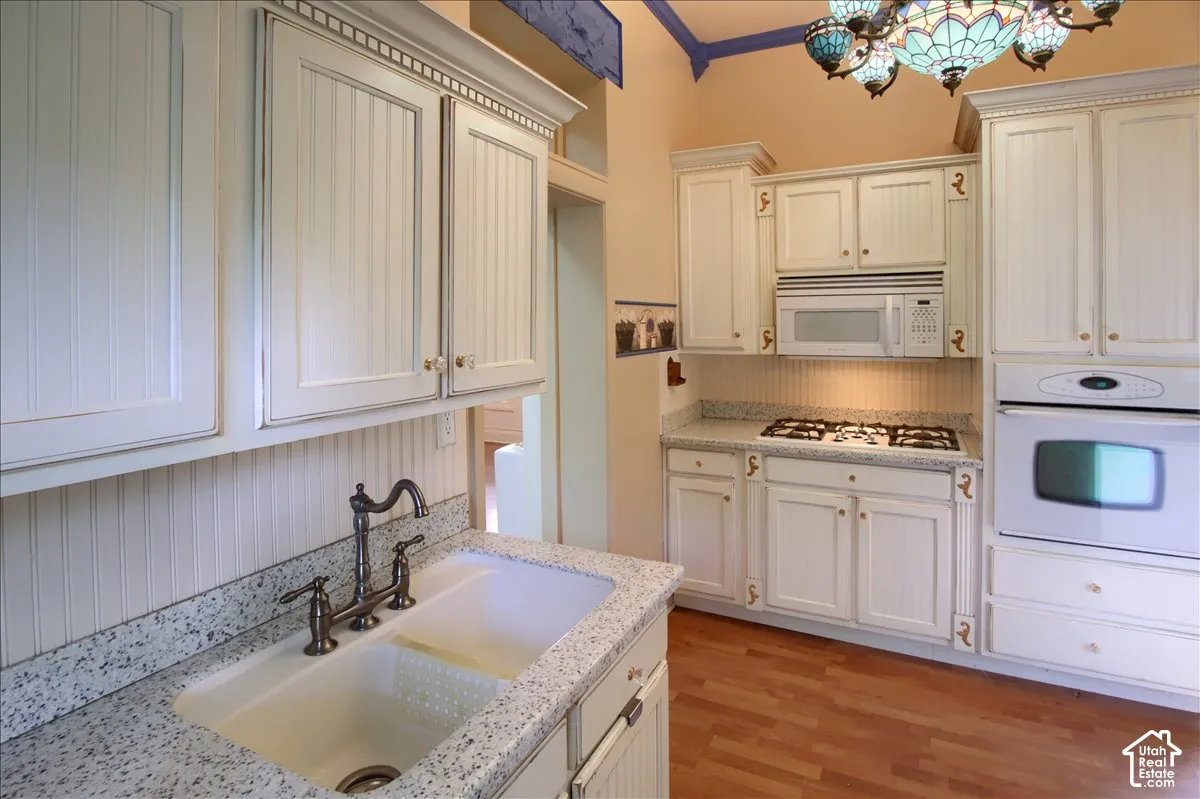 Kitchen featuring white beadboard cabinetry, stone-finish countertops, wood-finish flooring, integrated wall oven, and a decorative stained-glass chandelier
