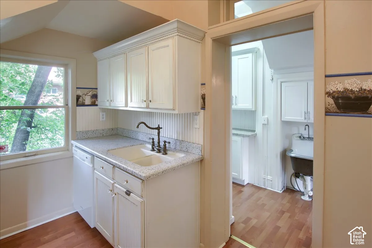 White cabinetry with beadboard detailing, stone-finish countertops, dual-basin undermount sink with bridge faucet, wood-finish flooring, and a wall-mounted utility sink