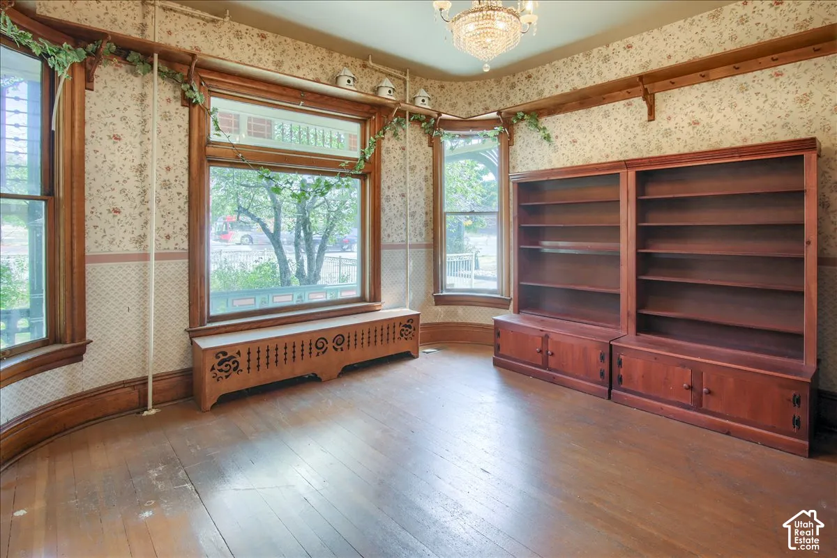 Room featuring wood-finish flooring, built-in wooden shelving, a decorative radiator cover, crown molding, and a crystal chandelier