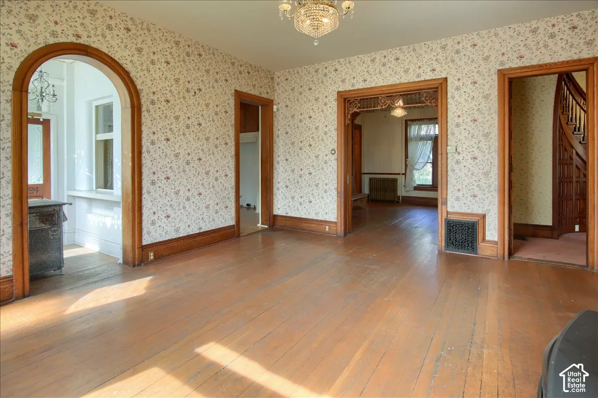Interior space featuring wood-finish flooring, an arched entryway, decorative wood millwork, a glass crystal chandelier, and patterned wallpaper