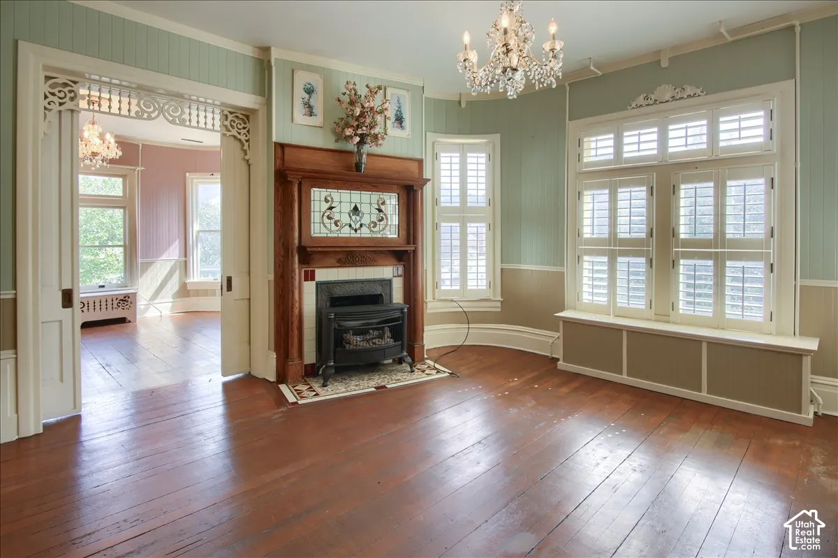 Wood-finish flooring, decorative wood fireplace mantel with stained-glass inlay, crystal chandelier, arched windows with interior shutters, and intricate door frame detailing
