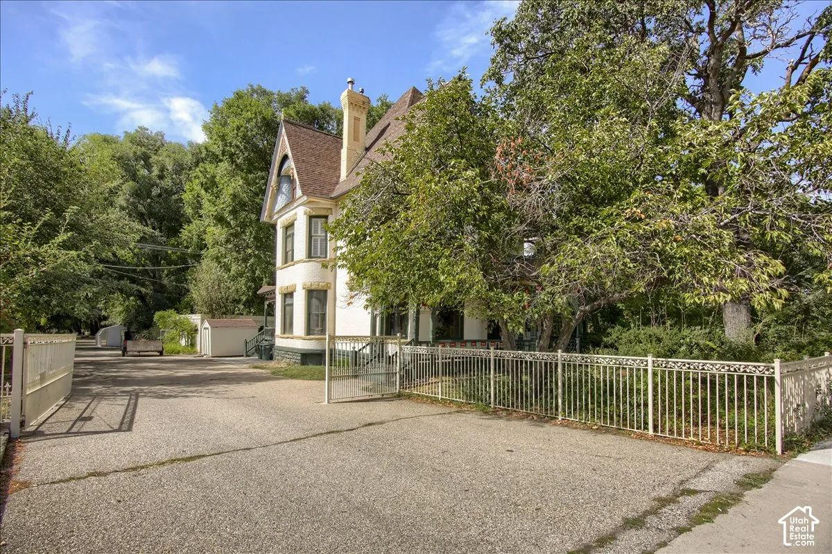 Victorian-style exterior featuring a steep gabled roof, intricate decorative trim, a light-toned facade with masonry detailing, and a gated driveway entry