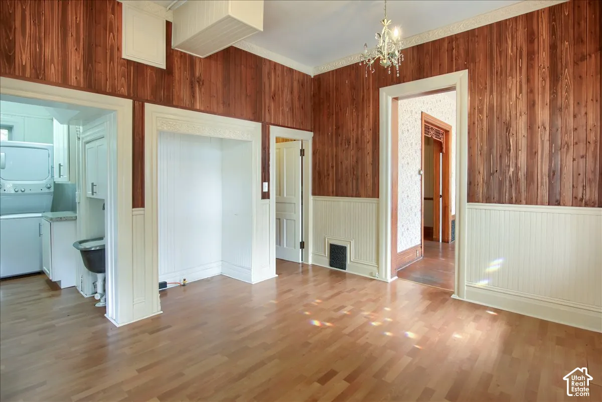 Room featuring vertical wood-paneled walls, wainscoting, wood-finish flooring, decorative crown molding, and a central light fixture