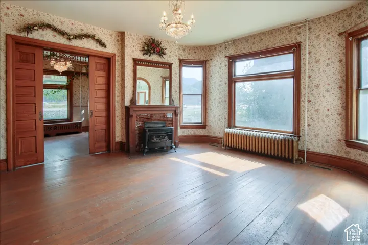 Hardwood flooring, wood-framed pocket doors, brick fireplace surround, decorative crystal chandelier, and large bay windows