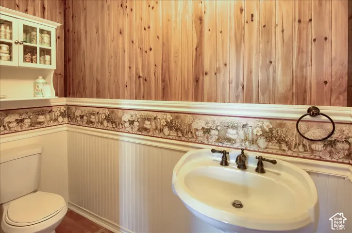 Vertical wood wall paneling, white beadboard wainscoting with decorative border, white wall-mounted upper cabinet with glass-front doors, pedestal sink with multi-handle metal faucet, and circular metal towel ring