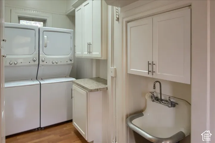Utility area featuring white shaker-style cabinetry, stone-finish countertops, wall-mounted utility sink with metal rim, and wood-finish flooring