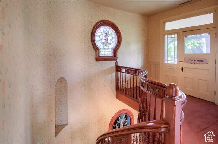 Curved wood staircase featuring ornate banisters, circular stained-glass windows, and a built-in arched wall niche