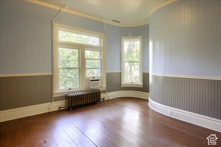 Curved wall featuring beadboard wainscoting, hardwood flooring, dual-pane windows, and a classic cast-iron radiator