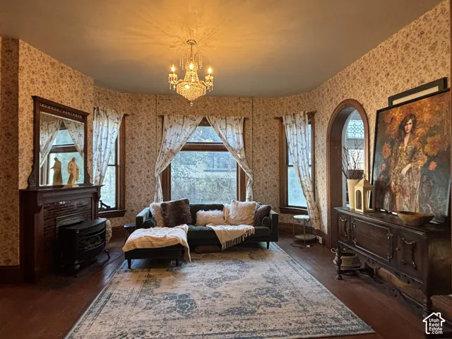 Bay window featuring wood-framed windows, a fireplace with a wood mantel, an arched doorway, and a crystal chandelier