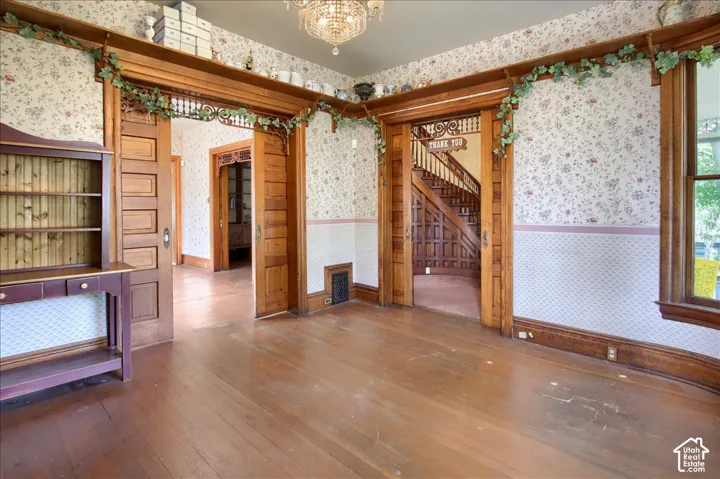 Wood-finish flooring, intricate natural wood door casings with decorative fretwork, wood-paneled pocket doors, patterned wallpaper with chair rail molding, and a crystal chandelier