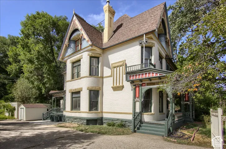 Victorian-style exterior featuring painted brick masonry, decorative gable detailing, ornate spindlework on the wrap-around porch, and a multi-level roofline
