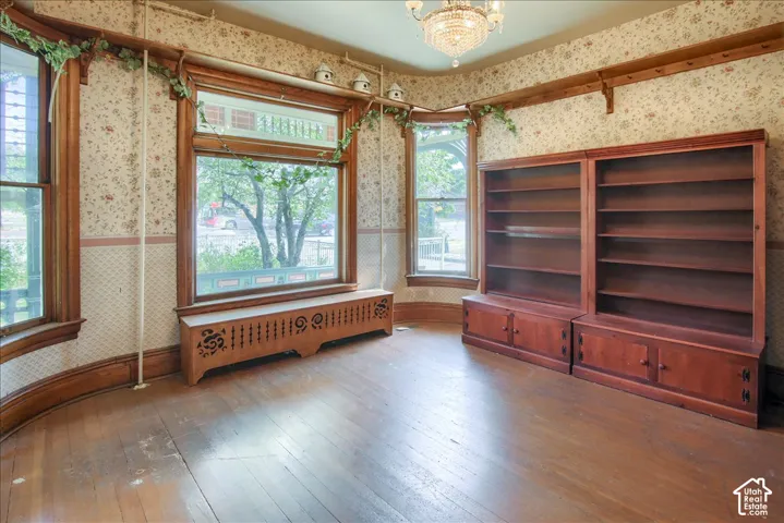 Room featuring wood-finish flooring, built-in wooden shelving, a decorative radiator cover, crown molding, and a crystal chandelier
