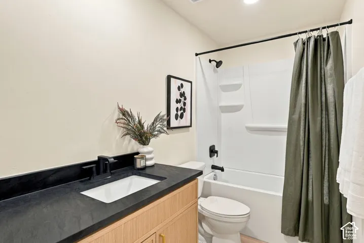Bathroom vanity with a dark countertop and integrated rectangular sink, wood-finish cabinetry, matte black hardware, and a white tub-shower combination