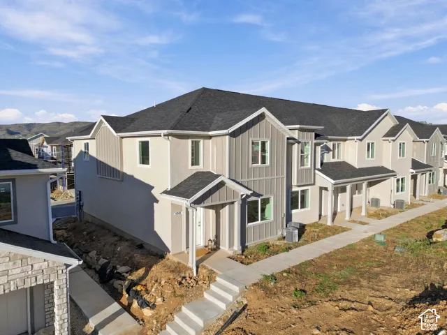 Multi-unit exterior featuring vertical board-and-batten siding, a dark-toned shingled hip roof, and concrete pathways