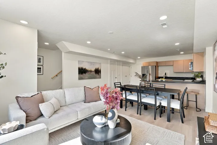 Open-concept living space featuring wood-finish flooring, recessed lighting, and kitchen cabinetry with a dark countertop and breakfast bar