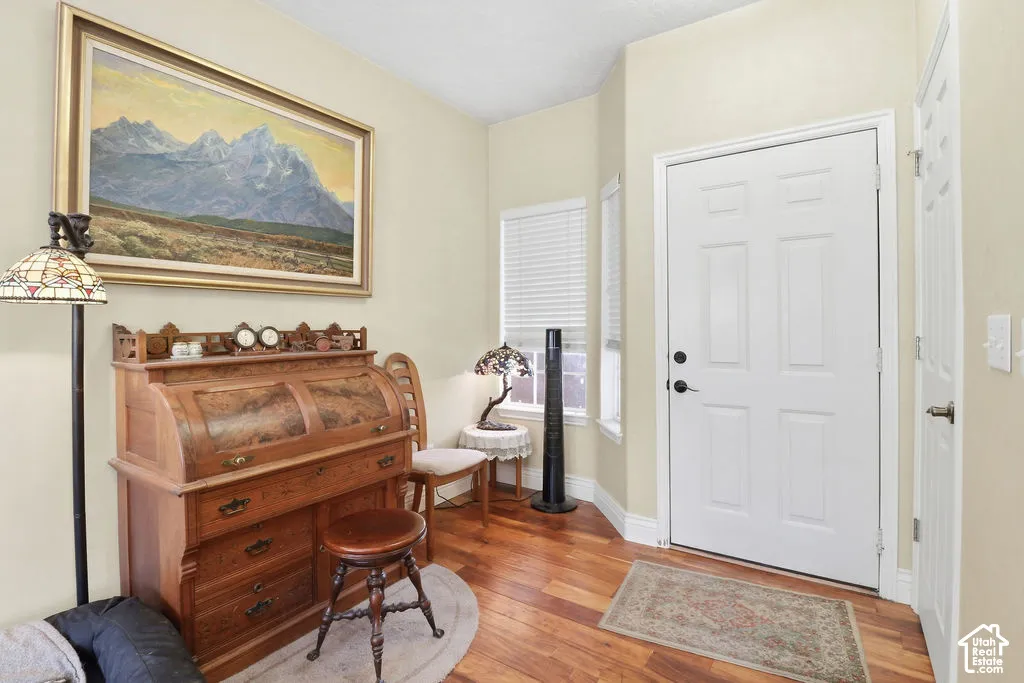 Entryway featuring wood-finish flooring, two vertical windows with integrated blinds, and a paneled entry door
