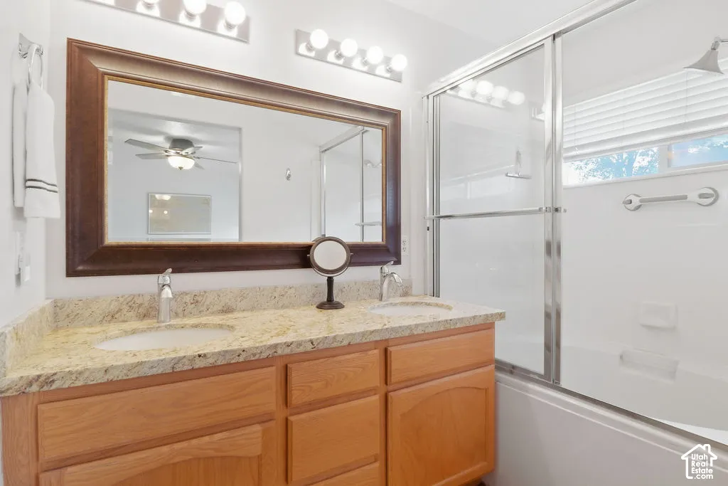 Double vanity featuring a stone-look countertop with dual undermount sinks, wood cabinetry, a large framed mirror, and a tub-shower combination with sliding glass doors