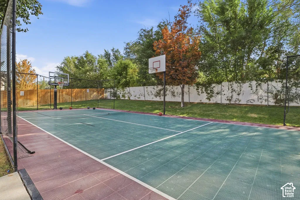 Multi-purpose sports court featuring integrated backboards, segmented modular surfacing, perimeter chain-link fencing, and wood-paneled privacy screens
