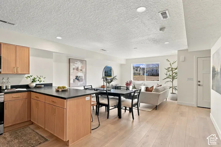 Kitchen area featuring light-toned wood cabinetry, dark solid-surface countertops, recessed lighting, and wood-finish flooring