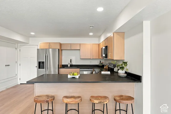 Kitchen featuring light-finish cabinetry, dark solid-surface countertops, wood-finish flooring, stainless steel appliances, and recessed lighting