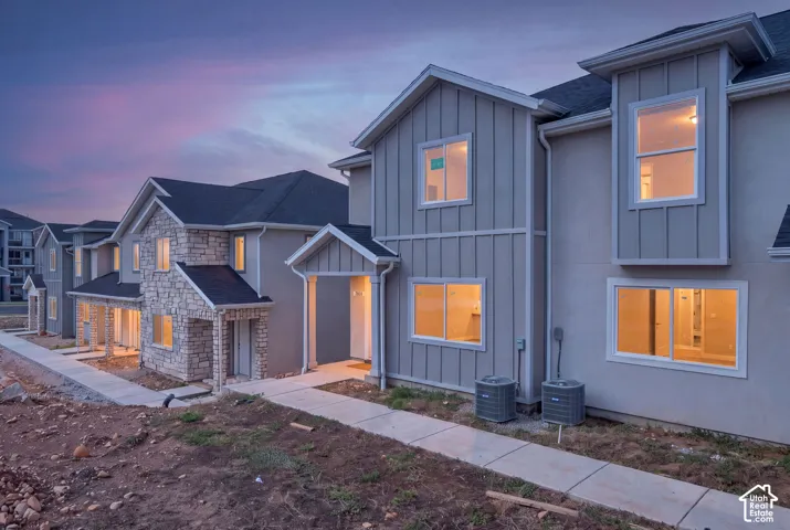 Multi-family exterior featuring board-and-batten siding, stone veneer accents, pitched rooflines, and concrete walkways