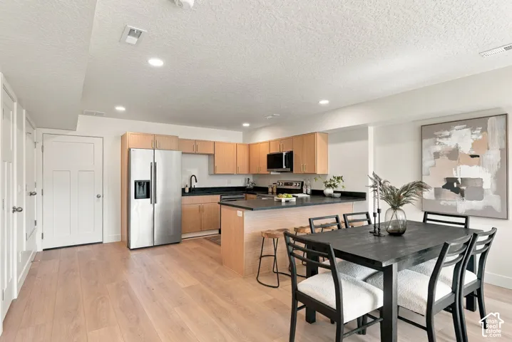 Kitchen featuring light wood-finish cabinetry, dark solid-surface countertops, stainless steel refrigerator, built-in microwave, and wood-finish flooring