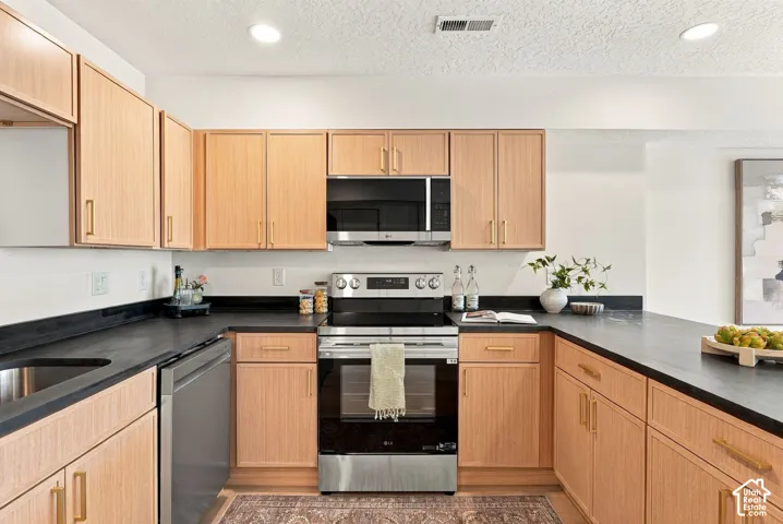 Kitchen featuring flat-panel wood-finish cabinetry, black countertops, brushed gold-tone hardware, and stainless steel appliances