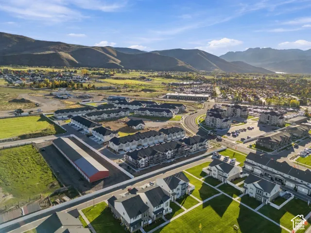 Aerial perspective of residential community featuring multi-story dwellings, paved roadways, manicured lawns, and prominent mountain backdrops