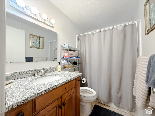 Bathroom featuring a wood-tone vanity, speckled stone-composite countertop with an integrated basin, large wall-mounted mirror, and a four-light fixture
