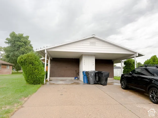 Exterior facade featuring a brick finish, white siding, and a covered carport with concrete surfacing