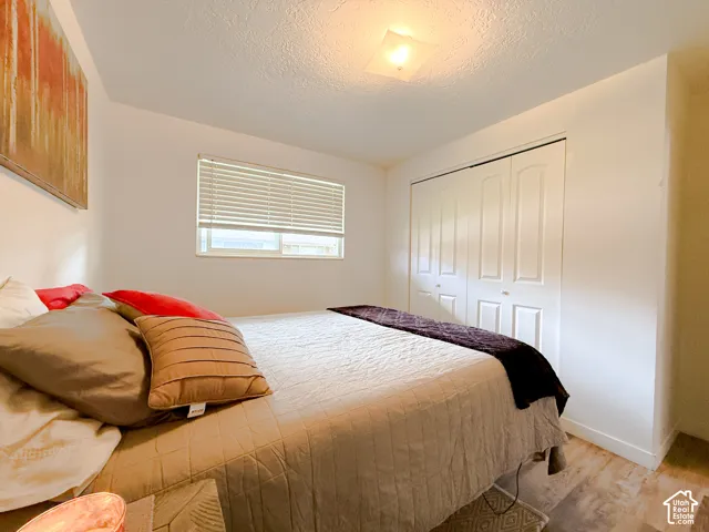 Bedroom featuring wood-finish flooring, white bi-fold closet doors, a single-pane window with horizontal blinds, and a centered flush-mount light fixture